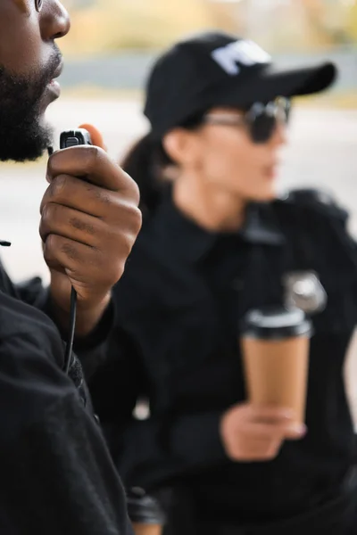 Policial afro-americano falando no rádio set com colega turvo no fundo ao ar livre — Fotografia de Stock