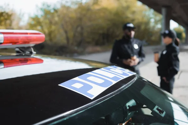 Auto con scritte della polizia vicino a poliziotti multiculturali su sfondo sfocato all'aperto — Foto stock