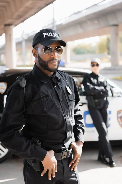 Confiant policier afro-américain regardant la caméra sur fond flou sur la rue urbaine — Photo de stock