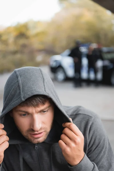 Scared hooded offender hiding with blurred police officers on background outdoors — Stock Photo