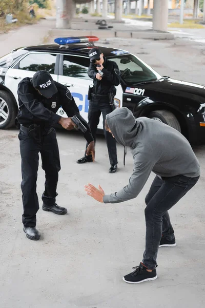 High angle view of multicultural police officers with pistols aiming at surrendered offender on blurred background outdoors — Stock Photo