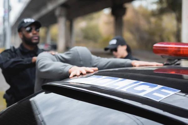 Patrol car with blue police lettering near multicultural enforce law officers arresting offender on blurred background outdoors — Stock Photo