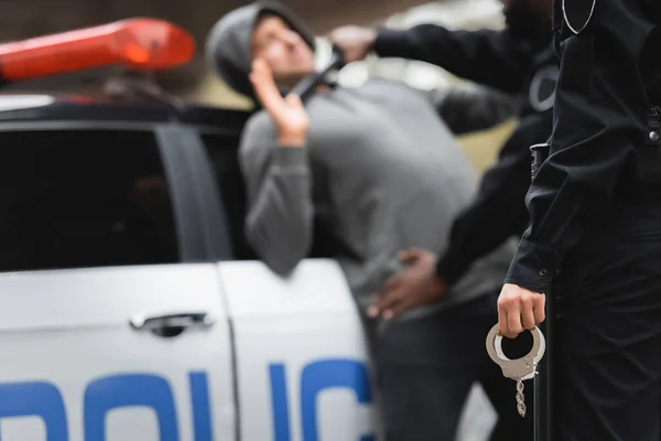 Женщина-полицейский, держащая наручники с размытым полисменом и преступником на заднем плане — стоковое фото