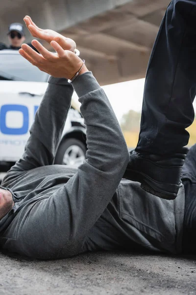 Policeman stepping on surrendered offender lying on street on blurred background — Stock Photo