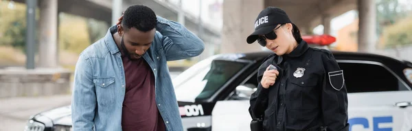 Policía hablando en la radio cerca de la víctima afroamericana sobre fondo borroso al aire libre, pancarta - foto de stock