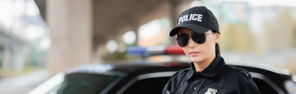 Ritratto di giovane poliziotta in occhiali da sole che guarda la fotocamera su sfondo sfocato all'aperto, banner — Foto stock