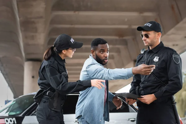 African american victim pointing with hand near police officers on blurred background on urban street — Stock Photo