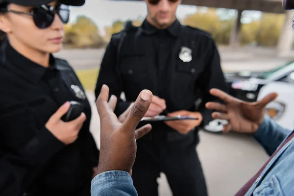 Negro americano hombre víctima gesto cerca policía oficiales en borrosa fondo al aire libre - foto de stock
