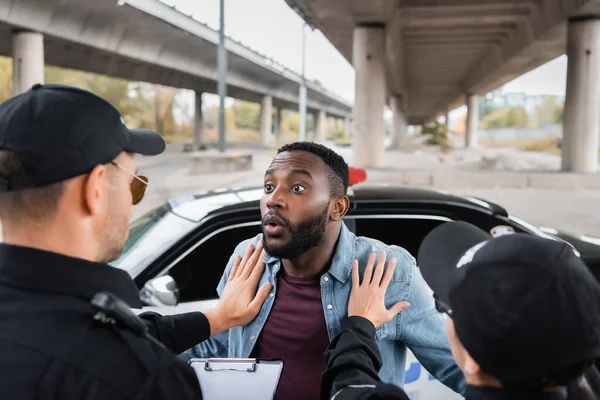 Vista posteriore di agenti di polizia calmante scioccato afro-americano vittima vicino pattuglia auto su sfondo sfocato all'aperto — Foto stock