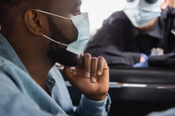 Autista afroamericano in maschera medica seduto vicino a poliziotta su sfondo sfocato — Foto stock