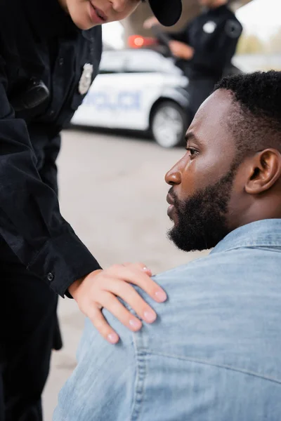 Víctima afroamericana mirando hacia otro lado cerca de oficial de policía en fondo borroso al aire libre - foto de stock