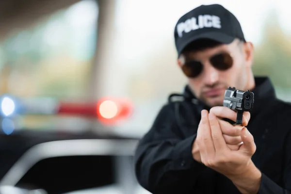 Pistola nas mãos de policial em óculos de sol no fundo borrado ao ar livre — Fotografia de Stock