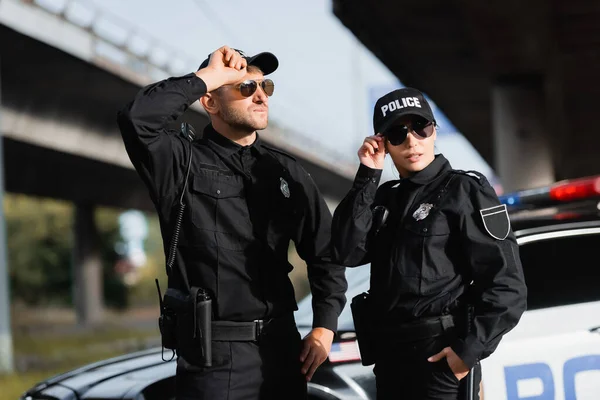 Police officers in sunglasses standing near car on blurred background outdoors — Stock Photo