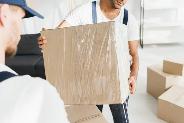 Indian mover holding wrapped in stretch film box near worker on blurred foreground — Stock Photo