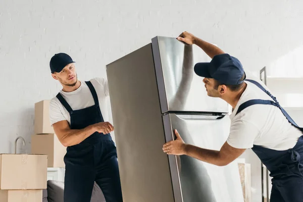 Mudanzas multiculturales en uniforme nevera móvil en apartamento - foto de stock