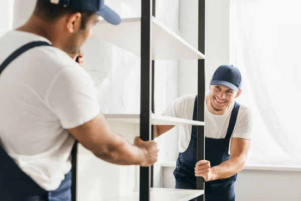 Feliz mover llevar pesado rack con indio compañero de trabajo en borrosa primer plano - foto de stock