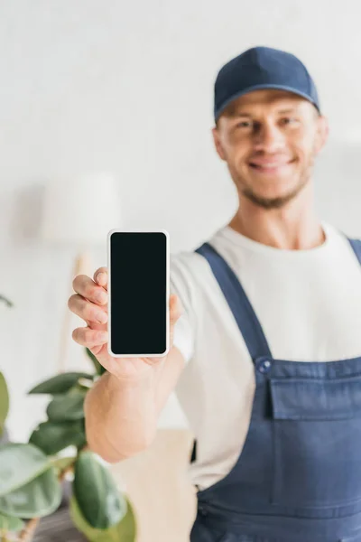 Smartphone with blank screen in hand of cheerful mover in uniform — Stock Photo