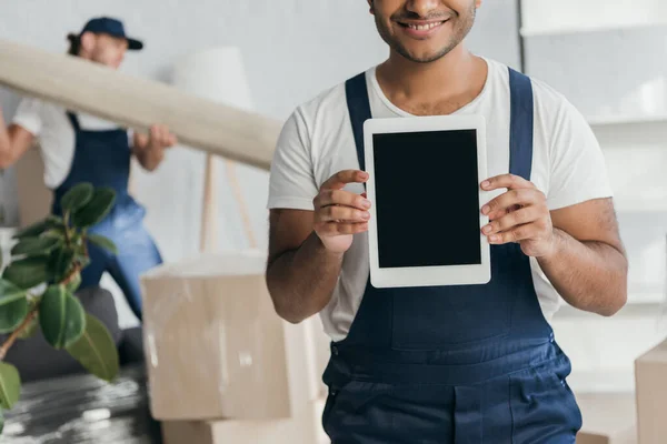 Abgeschnittene Ansicht eines glücklichen indischen Arbeiters in Uniform, der ein digitales Tablet mit leerem Bildschirm in der Nähe des Mover hält, der Teppich auf verschwommenem Hintergrund hält — Stockfoto