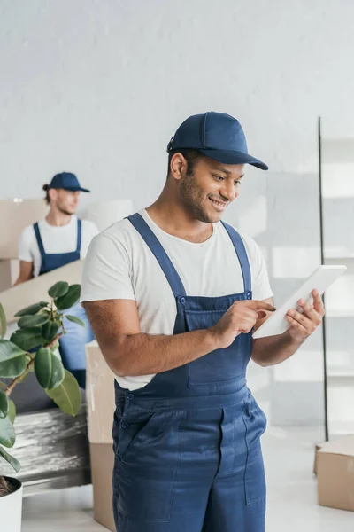 Trabalhador indiano alegre em uniforme usando tablet digital perto de mover em fundo turvo — Fotografia de Stock