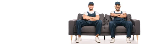 Full length of cheerful multicultural movers sitting on sofa with crossed arms and smiling on while, banner — Stock Photo