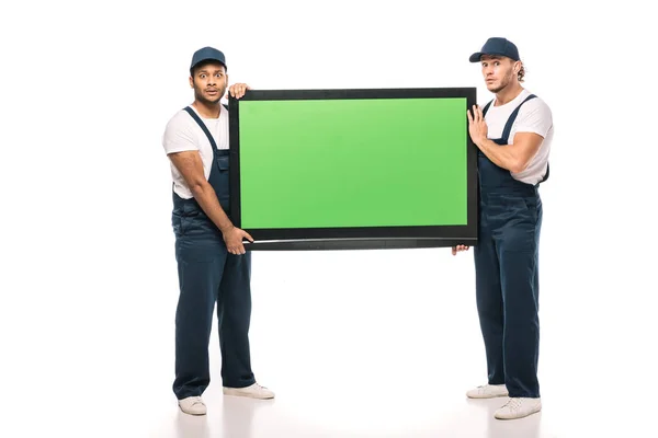 Comprimento total de movimentadores multiculturais chocados transportando tv plasma com tela verde no branco — Fotografia de Stock