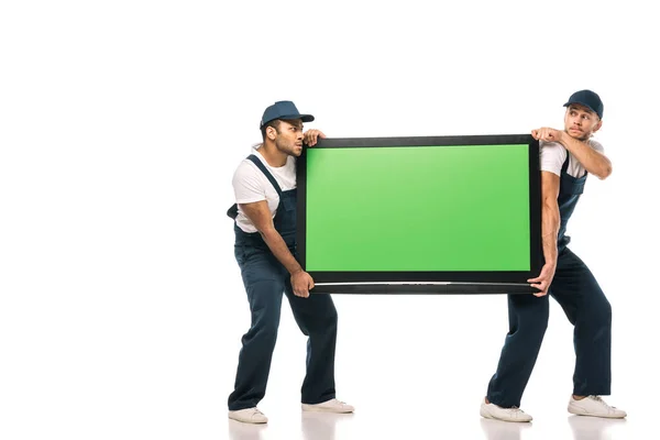 Full length of multicultural movers stealing plasma tv with green screen on white — Stock Photo