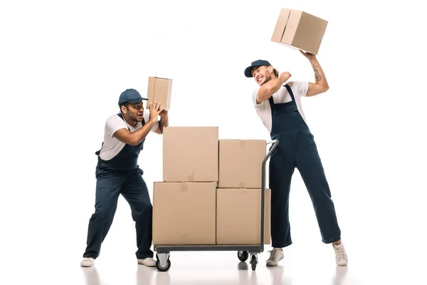 Volle Länge des wütenden tätowierten Mover in Uniform hält Karton in der Nähe verängstigten indischen Mitarbeiter und Hand LKW mit Paketen auf weiß — Stockfoto