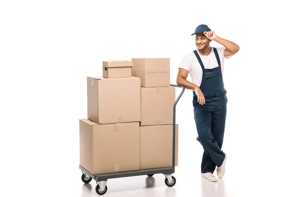 Joyeux déménageur indien debout près du camion à main avec boîtes en carton et bouchon de réglage sur blanc — Photo de stock