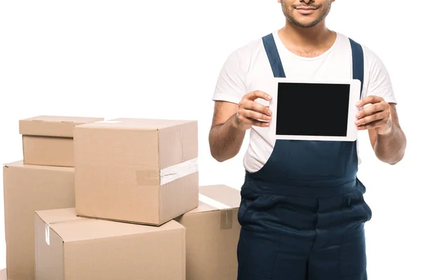 Vista recortada de movimiento indio feliz en overoles que sostienen la tableta digital con la pantalla en blanco cerca de cajas de cartón aisladas en blanco - foto de stock