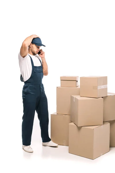 Полная длина тележки в униформе и шапочка пыхтя щеки во время разговора на смартфоне возле коробки коробки на белом — стоковое фото