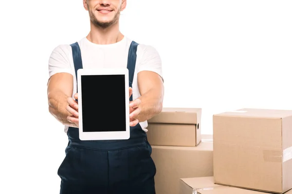 Vista parcial de alegre mover en uniforme celebración tableta digital con pantalla en blanco cerca de cajas de cartón aislado en blanco - foto de stock