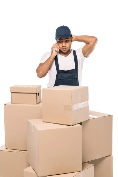 Shocked indian mover in overalls talking on smartphone and looking at carton boxes isolated on white — Stock Photo