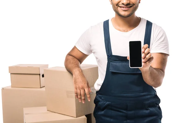 Vista cortada de feliz indiana mover em macacões segurando smartphone com tela em branco perto de caixas de papelão isolado no branco — Fotografia de Stock