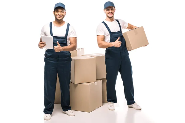 Full length of cheerful indian worker holding digital tablet and standing with mover while showing thumbs up near boxes on white — Stock Photo