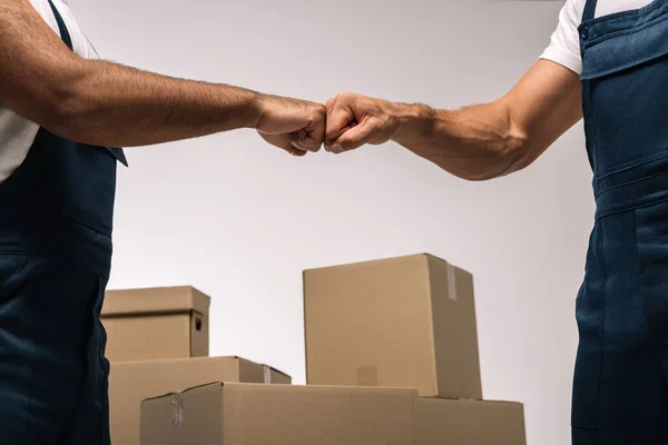 Cropped view of workers bumping fists near boxes on grey — Stock Photo
