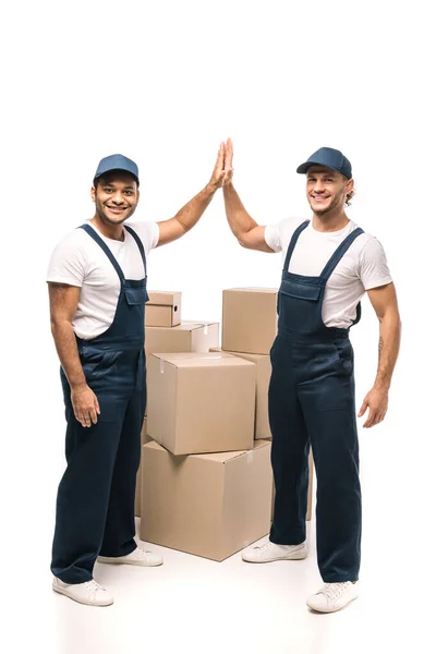 Повна довжина щасливих мультикультурних працівників, які дають високі п'ять біля коробок на білому — стокове фото