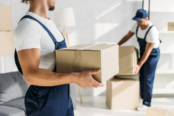 Cropped view of mover holding box near indian coworker on blurred background — Stock Photo