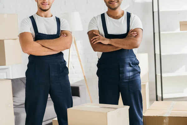 Cropped view of multicultural movers standing with crossed arms near boxes — Stock Photo
