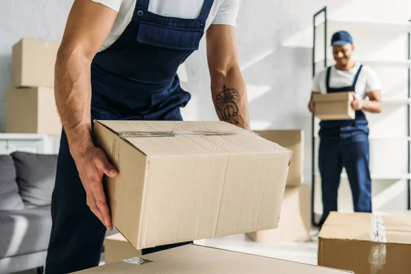 Cropped view of tattooed worker in uniform holding carton box near indian coworker — Stock Photo