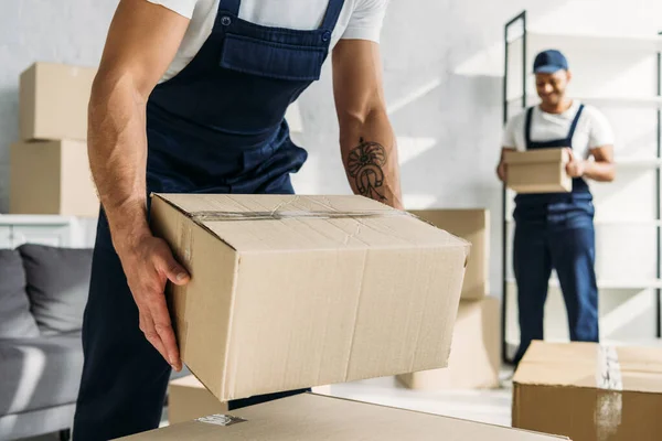 Vista cortada de trabalhador tatuado em caixa de papelão uniforme perto de colega de trabalho indiano — Stock Photo