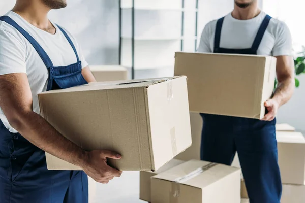 Vista cortada de movers multiétnicos em caixas de transporte uniformes no apartamento — Stock Photo