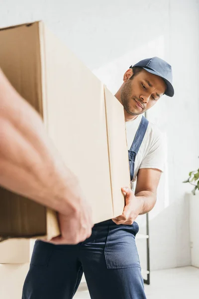 Déménageur indien en uniforme portant une énorme boîte en carton avec un collègue au premier plan flou — Photo de stock