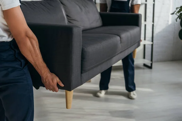 Partial view of workers carrying heavy sofa in apartment — Stock Photo