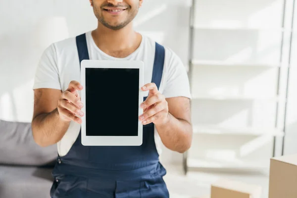 Abgeschnittene Ansicht eines lächelnden indischen Arbeiters in Uniform, der ein digitales Tablet mit leerem Bildschirm in der Wohnung hält — Stockfoto