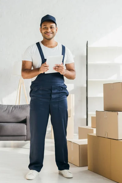 Volle Länge der fröhlichen indischen Arbeiter in Uniform hält digitale Tablette in der Wohnung — Stockfoto