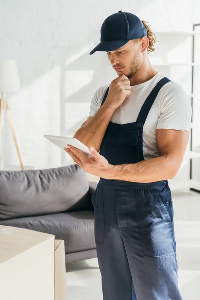 Pensive mover in uniform holding digital tablet in apartment — Stock Photo