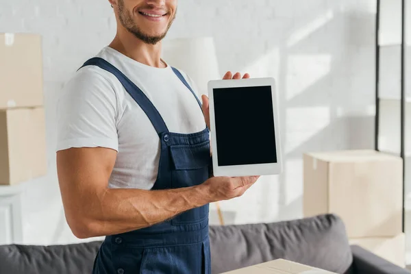 Vista ritagliata di allegro traslocatore in uniforme azienda tablet digitale con schermo bianco in appartamento — Foto stock