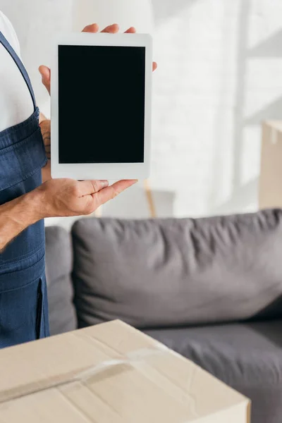 Vista recortada de mover en uniforme celebración tableta digital con pantalla en blanco en el apartamento - foto de stock