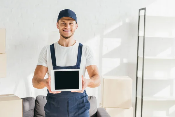 Cheerful mover in uniform holding digital tablet with blank screen in apartment — Stock Photo