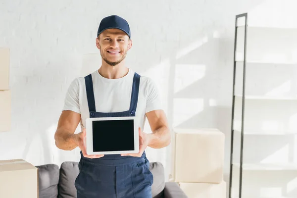 Alegre mover en uniforme celebración tableta digital con pantalla en blanco en apartamento - foto de stock